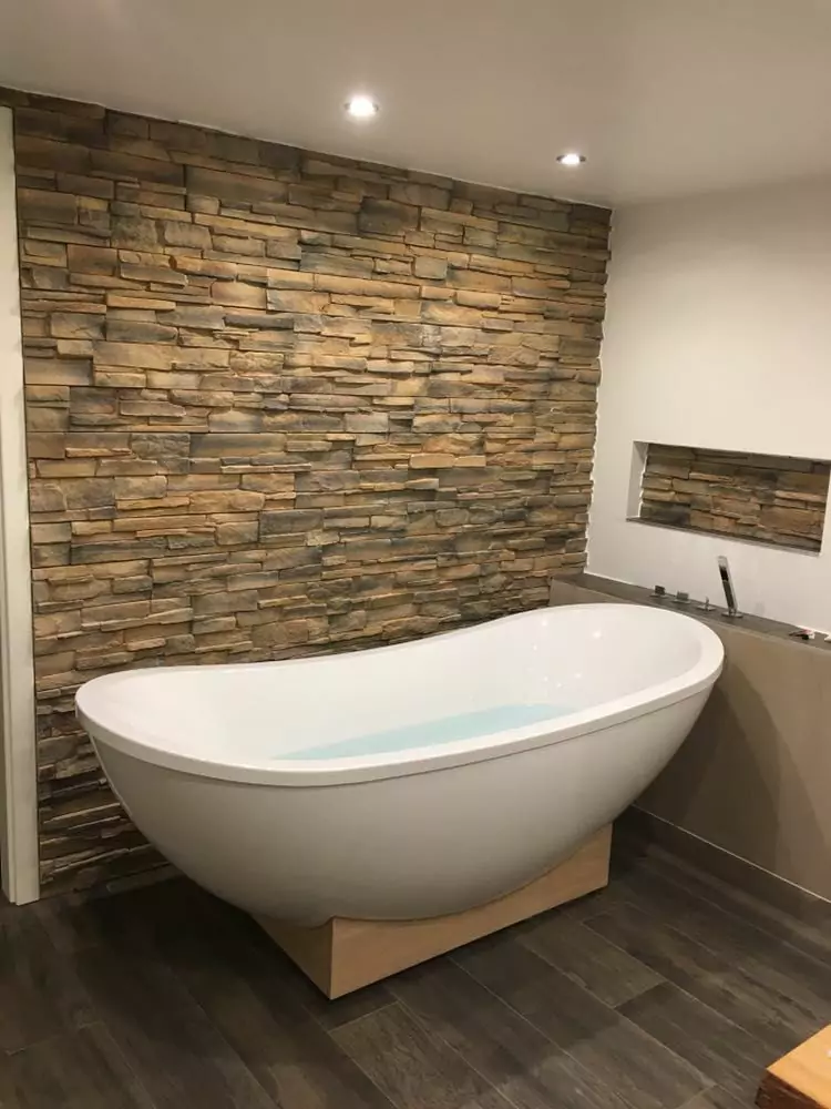 Freistehende weiße Badewanne vor einer Natursteinwand