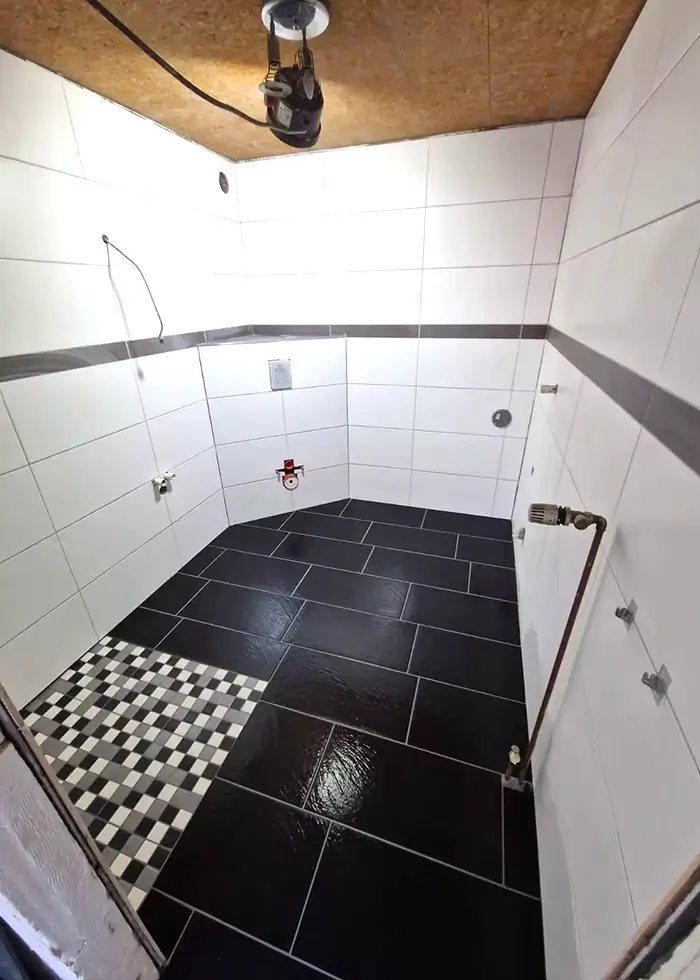 Badezimmer im Rohbau, weiße Fliesen wurden an den Wänden verlegt und schwarze Bodenfliesen